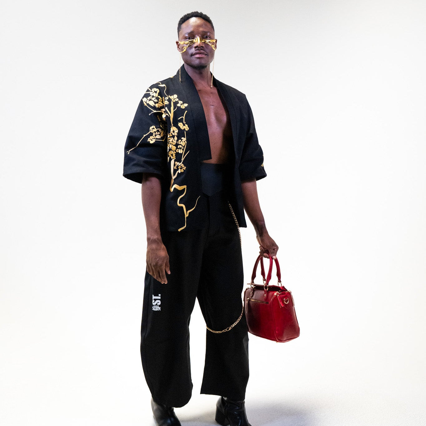 Yelsh model wearing the YST limited edition black kimono with gold patterns of cherry blossom, holding a red bag on a white background